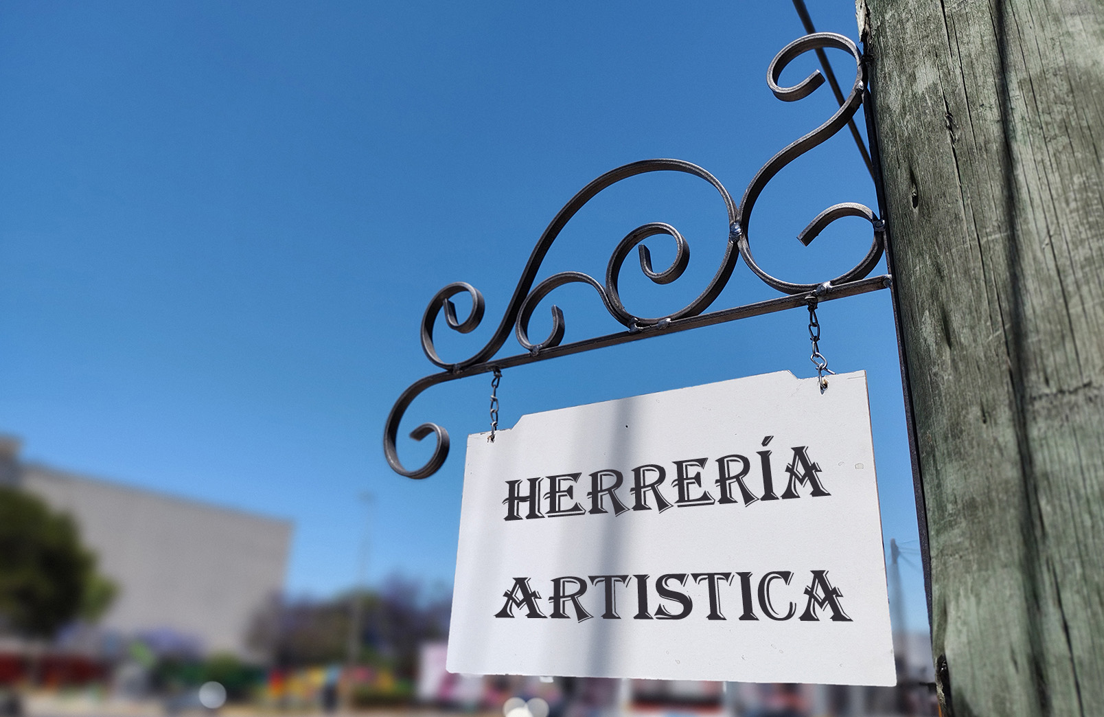 Cartel de Herrería Artística suspendido de un soporte de hierro con rulos decorativos